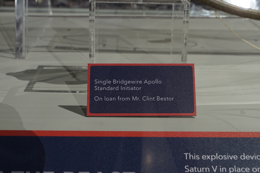 The sign accompanying the Saturn V holddown arm single bridgewire Apollo Standard initiator in the Apollo:  When We Went to the Moon exhibit